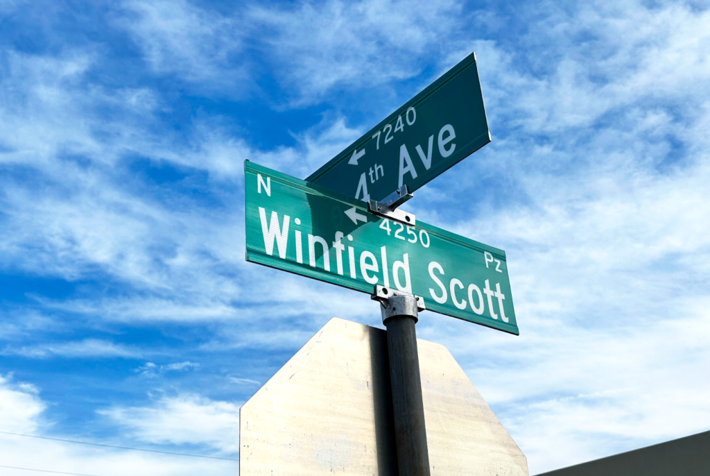 Intersection street signs showing Winfield Scott Pz and 4th Ave N mounted perpendicular to each other on post against blue sky